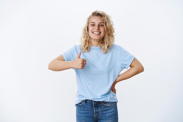 Free photo great, good job. portrait of grinning cute and friendly charismatic attractive blonde with blue eyes smiling pleased as showing thumb up in approval and like, giving positive opinion on white wall.