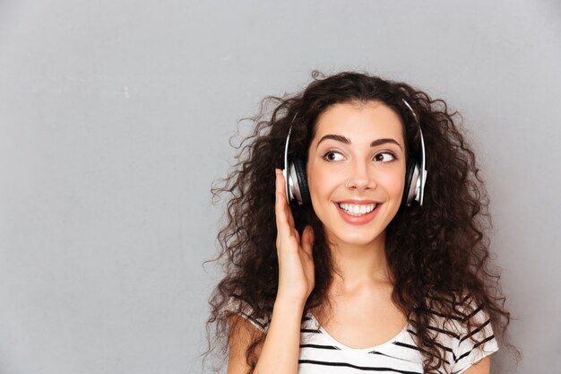 Free Photo great picture of curly caucasian woman in striped t shirt in headphones enjoying music via modern device while resting 