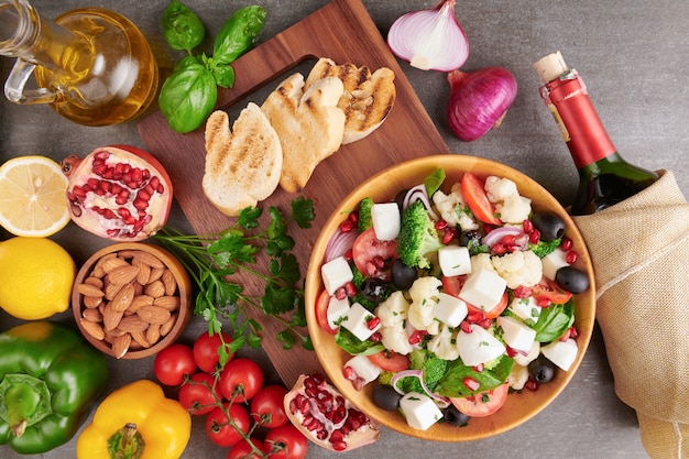 Free photo greek salad or horiatiki with large pieces of tomatoes, cucumbers, onion, feta cheese and olives in white bowl isolated top view. village salad with diced mozzarella, arugula, parsley and olive oil