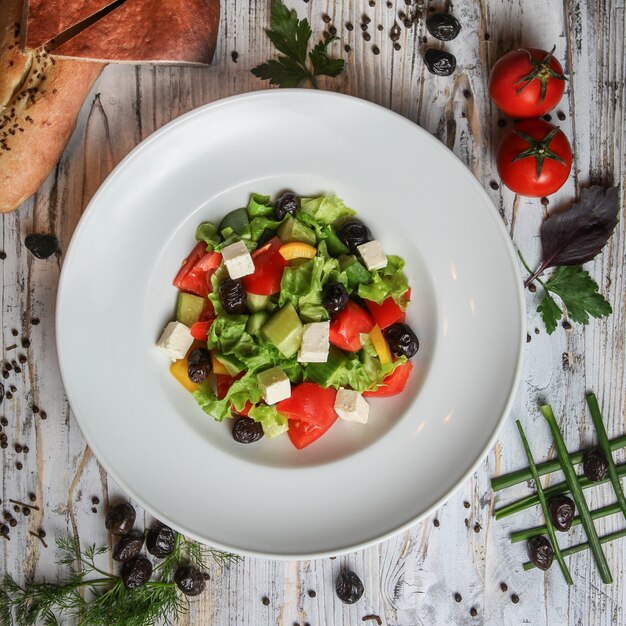 Greek salad in a plate with tomato, olives, bread, herbs and spices