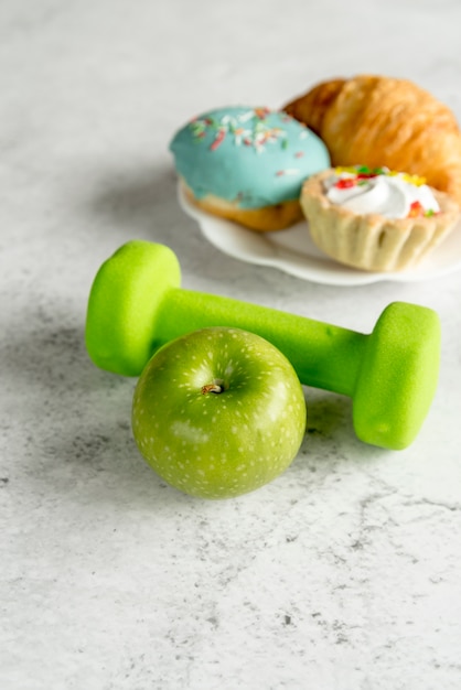 Free photo green apple and dumbbell with sweet food on concrete backdrop