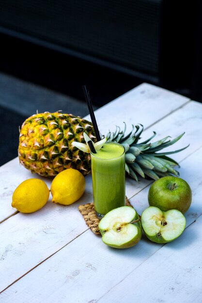 Green apple juice served with apple, pineapple and lemons on white wood table