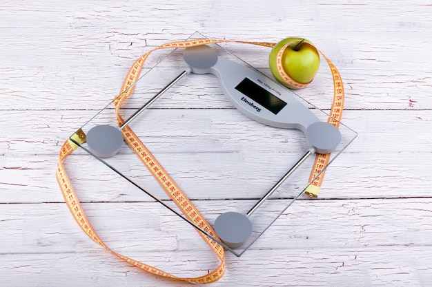 Green apple, orange  tape-measure lie on glass weighing scales