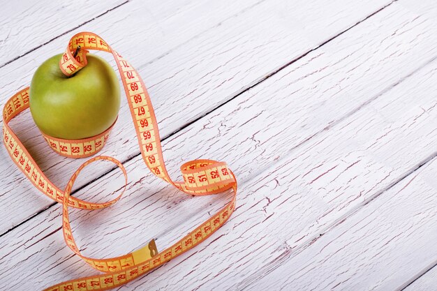 Green apple and orange tape-measure lie on white wooden floor