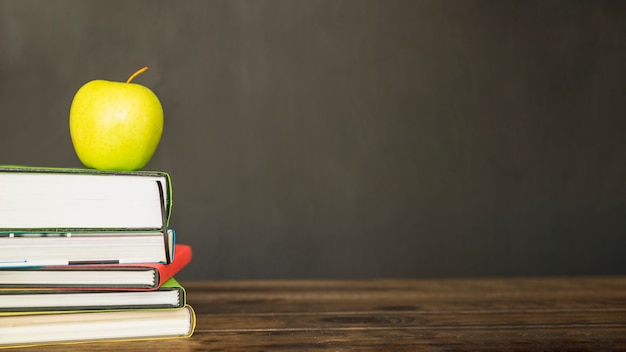 Green apple on pile of books on desk