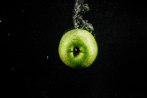 Free photo green apple splashes water falling on black background