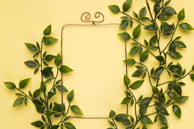 Free Photo green artificial leaves near the empty frame on yellow backdrop