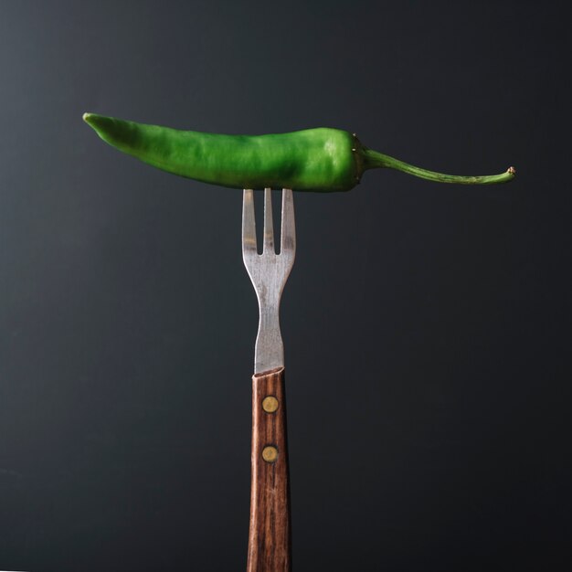 Green chili pepper in fork on black backdrop