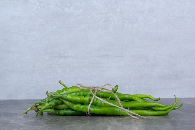 Green chili peppers tied with rope on marble table.