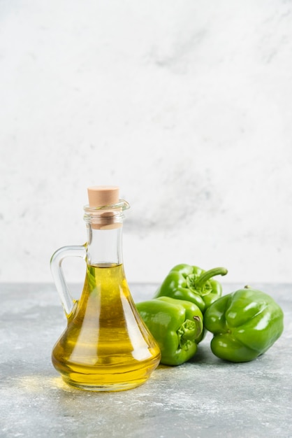 Free photo green chili peppers with a bottle of extra virgin olive oil on marble table.