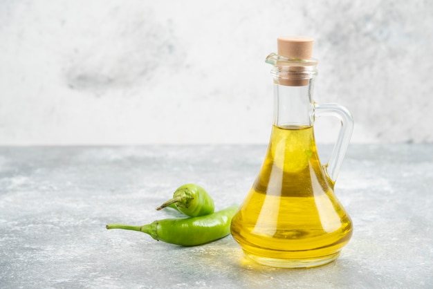 Free photo green chili peppers with a bottle of extra virgin olive oil on marble table.