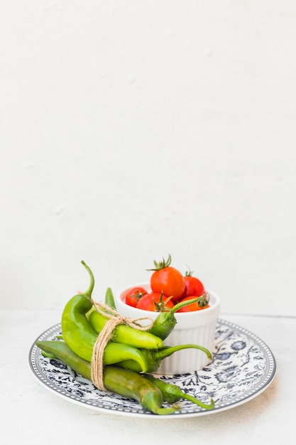 Free photo green chilies and bowl of red tomatoes on ceramic plate against white background