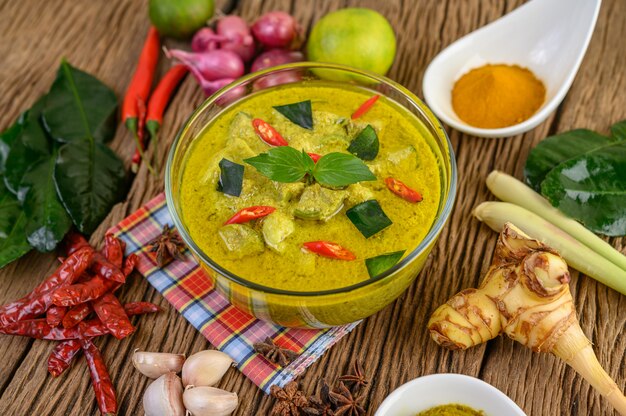 Green curry in a bowl and spices on wooden table.