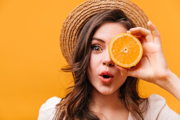 Free photo green-eyed girl with wavy hair looks at camera in surprise and covers her eye with orange.