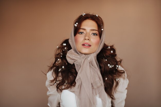 Green-eyed woman in white blouse and with small flowers in hair posing. woman in headscarf looks at camera.