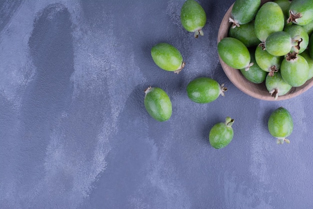 Free photo green feijoa fruits in a wooden cup on blue table.