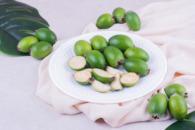 Green feijoas in a white plate with leaves around