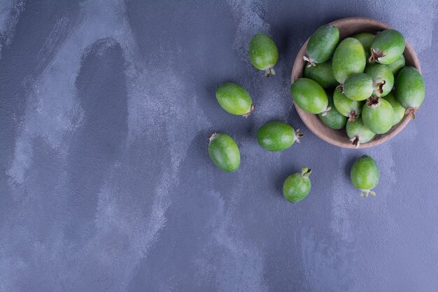 Green feijoas in a wooden cup on blue surface