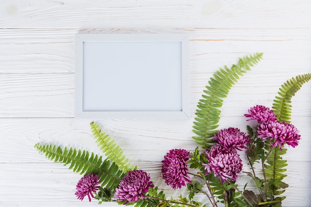 Green fern leaves with purple flowers and frame on table