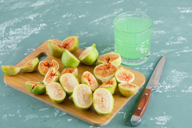 Free photo green figs with drink, knife on plaster and cutting board, top view.