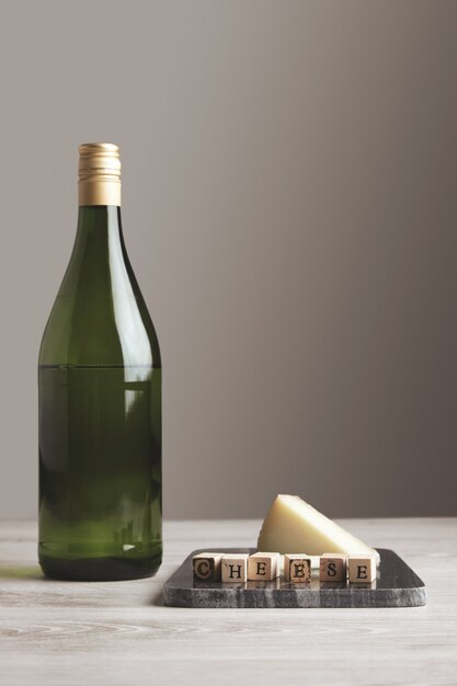 Green grape wine juice bottle near stone marble board with wooden letters cheese and goat cheese on it isolated on white blank backround and table