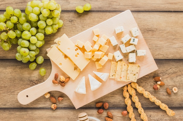 Green grapes, almonds, bread sticks and cheese blocks on chopping board over wooden desk