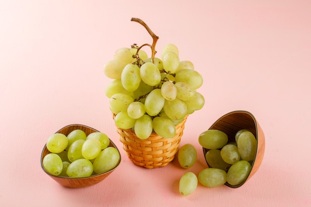 Green grapes in bowls and wicker basket on a pink. high angle view.