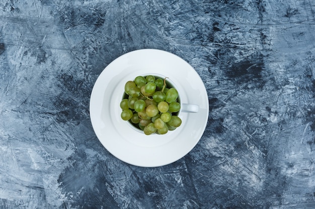 Green grapes in a white cup with plate top view on a grungy plaster background