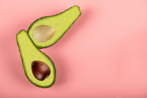 Green half avocadoes isolated on pink wall, with and without seed