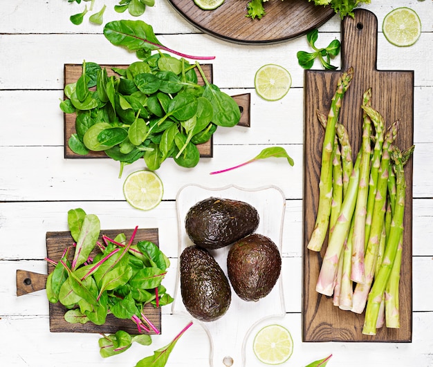 Free photo green herbs, asparagus and black avocado on a white wooden background. top view. flat lay