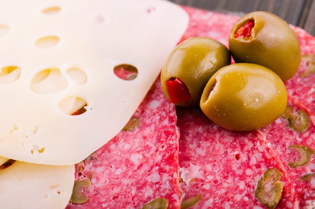 Green olives lie on sliced Swiss cheese and salami