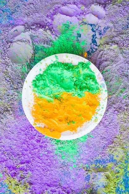 Green and orange holi powder on plate over the backdrop