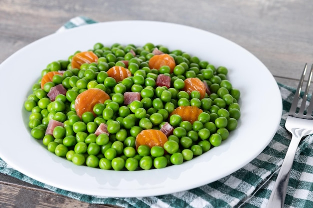 Free Photo green peas with serrano ham and carrot on wooden table