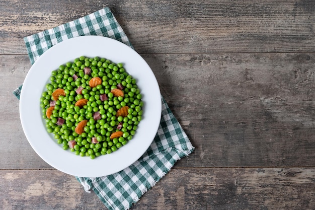 Free Photo green peas with serrano ham and carrot on wooden table