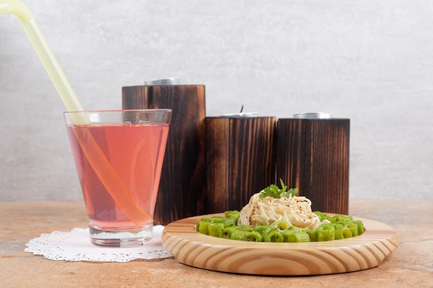 Green penne pasta and vermicelli on wooden plate with glass of juice