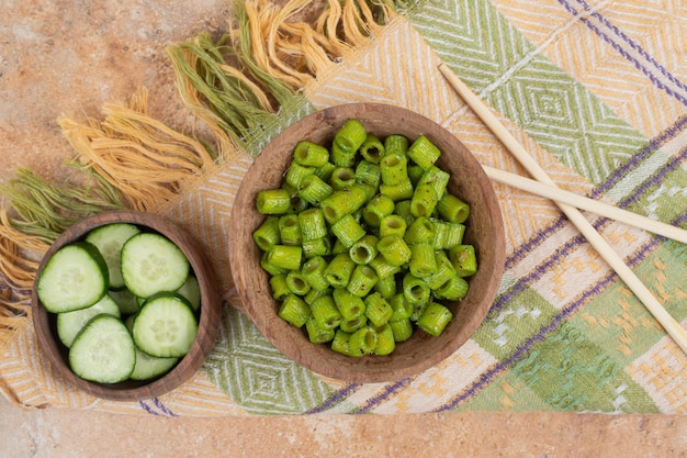 Green penne pasta with cucumber slices on tablecloth. 