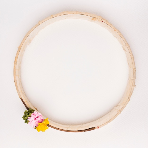 Free Photo green; pink and yellow flowers on wooden circular frame against white backdrop