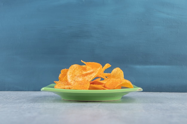 Green plate of spicy chips placed on stone.