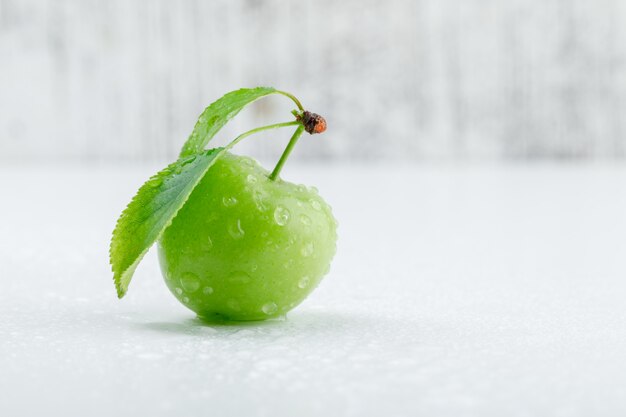 Green plum with leaves on grungy and white wall, side view.