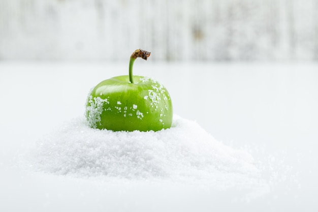 Free photo green plum with salt crystals on white and grungy wall, side view.