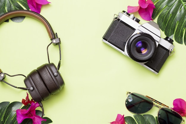 Free photo green surface with retro camera, headphones and glasses with tropical flowers