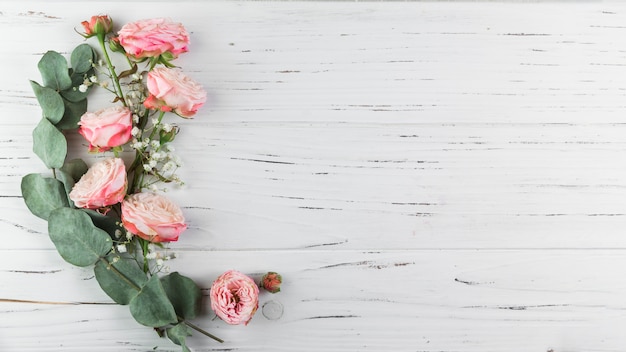 Green twig; pink roses and white gypsophila on white wooden textured background