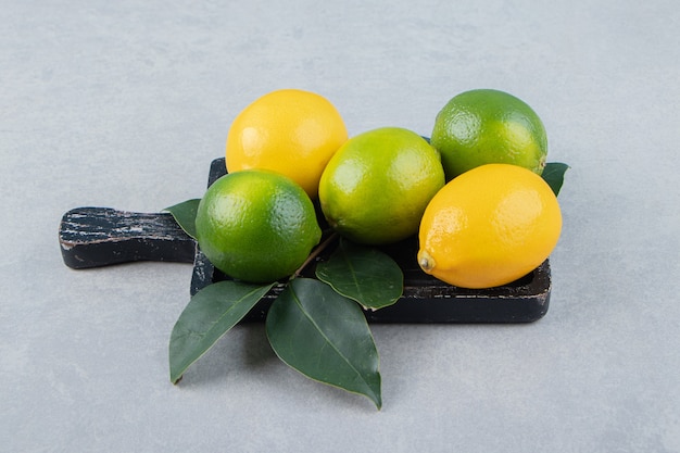 Green and yellow lemons on black cutting board. 