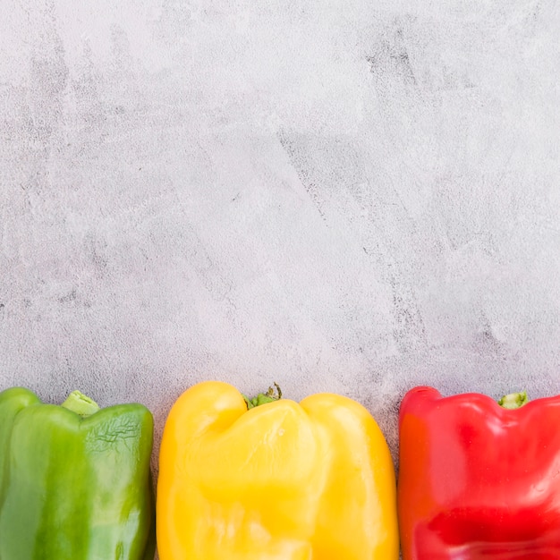 Green; yellow and red bell pepper on grey concrete backdrop