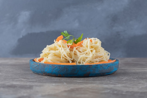 Greens and grated carrot on spaghetti, on the wooden board , on the marble.