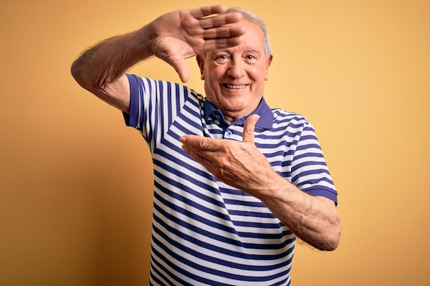 Free photo grey haired senior man wearing casual navy striped tshirt standing over yellow background smiling making frame with hands and fingers with happy face creativity and photography concept