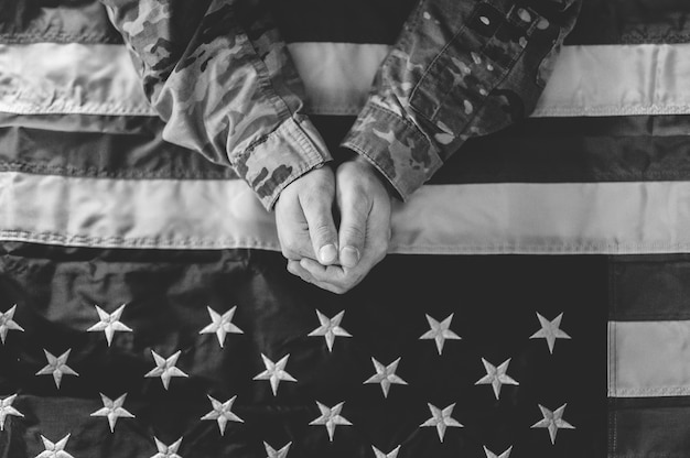 Free photo greyscale shot of an american soldier mourning and praying with the american flag in front of him