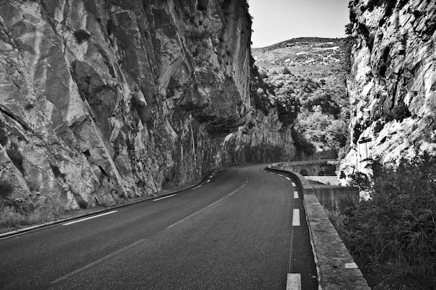 Greyscale shot of an empty road surrounded by rocks under the sunlight at daytime