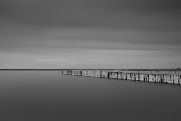 Greyscale shot of a long pier near the sea under the storm clouds