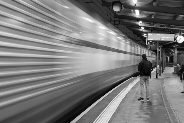 Free photo greyscale shot of a man waiting for a train in the station and a blurred train in the motion